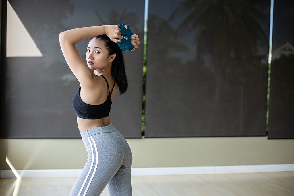 Women exercise with dumbbell weight plates and twist to the back.