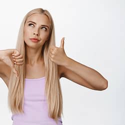 Thoughtful blond girl shows thumbs up and down, making decision, weighing pros and cons